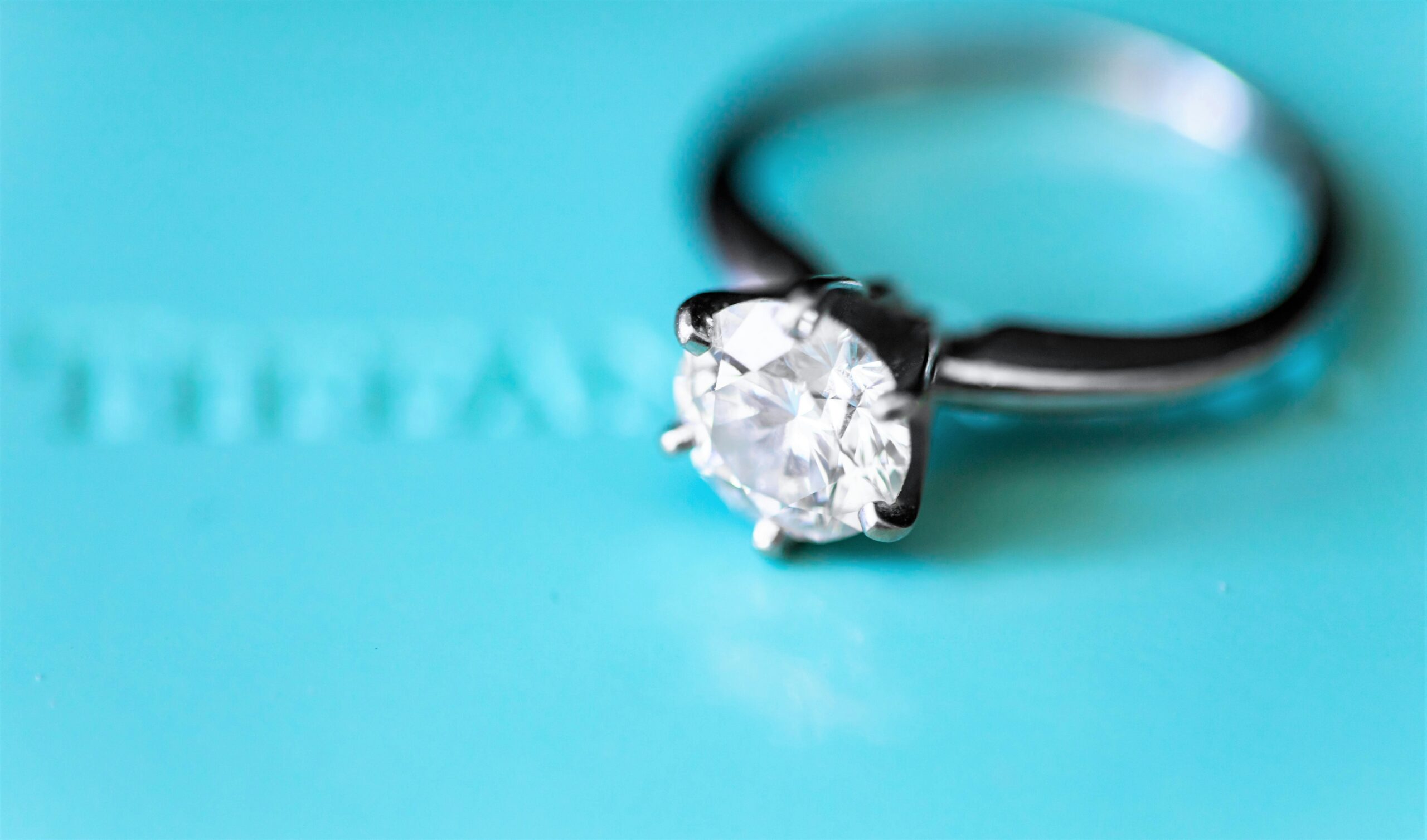 A diamond engagement ring sitting on a blue surface